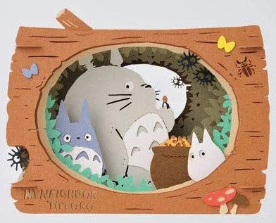 A beautifully crafted Paper Theater kit featuring Totoro and friends inside a log. The intricate design showcases Totoro surrounded by two smaller Totoros and various forest elements, including mushrooms, flowers, and insects. This DIY craft displays a charming scene from 'My Neighbor Totoro', perfect for fans of Studio Ghibli and paper art.