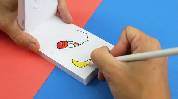 A person uses a white pencil to color a yellow crescent moon in a flipbook. The flipbook features simple, outlined designs, including a pencil with a red eraser. The background is split into pink and blue sections.
