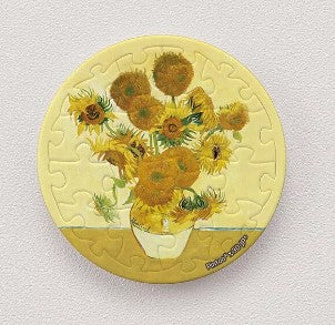 A circular jigsaw puzzle featuring Vincent van Gogh's iconic 'Sunflowers' painting. The image showcases vibrant yellow sunflowers in a white vase set against a warm, muted background. Each piece of the puzzle is magnetic, making it perfect for display or fun solving.