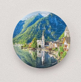 A circular jigsaw puzzle featuring the picturesque Lakeside Village of Hallstatt, Austria. The image showcases vibrant buildings reflecting on the serene waters of the lake, with lush green mountains in the background, embodying the beauty of this iconic destination.