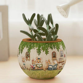 A colorful 3D jigsaw puzzle in the shape of a flower pot, featuring adorable cartoon mice reading books in a garden setting, surrounded by green leaves. The pot is designed to resemble a friendly outdoor scene, making it a delightful decorative piece.