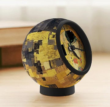 A 3D jigsaw puzzle clock featuring Gustav Klimt's famous artwork 'The Kiss'. The clock is spherical with a mosaic-like pattern in vibrant gold and black hues, showcasing intricate details of the artwork. It stands on a round base, making it a unique decorative piece for any room.