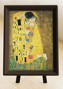 A completed 150-piece jigsaw puzzle of Gustav Klimt's famous painting 'The Kiss'. The puzzle is displayed in a framed stand, showcasing vibrant colors and intricate designs, highlighting the intimate embrace of the couple surrounded by golden hues and floral patterns.