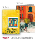 Les Rues Tranquilles A5 notebook cover featuring a vibrant yellow and blue window and a charming street scene with a person holding an umbrella, designed by Pintoo. The back showcases a bicycle graphic, enhancing its artistic appeal.