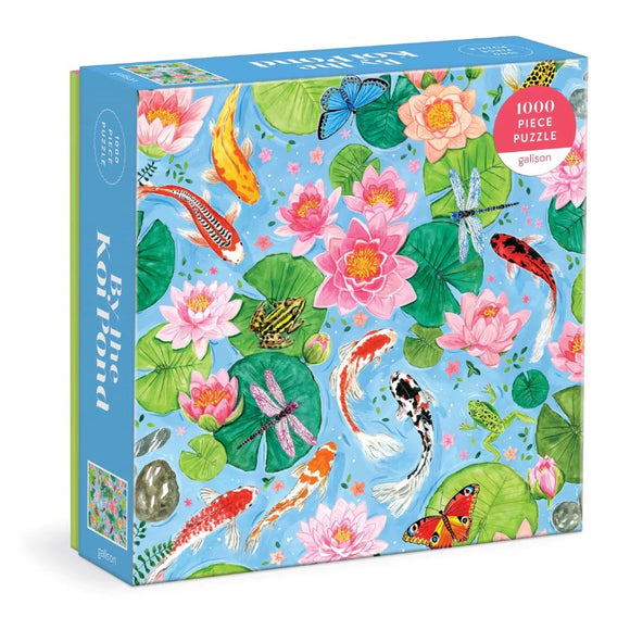 The packaging for the 'By The Koi Pond' jigsaw puzzle from Galison, featuring a vibrant illustration filled with colorful koi fish, blooming water lilies, dragonflies, and frogs against a blue background. The box clearly states it contains 1000 pieces, making it an engaging and artistic puzzle for nature and art lovers.
