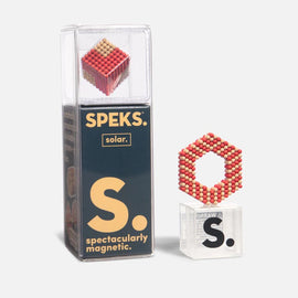 A clear packaging for the Speks Elements: Solar set, featuring a vibrant magnetic cube made up of small colored spheres. Next to it is a hexagonal shape created from the same magnetic spheres, demonstrating the product's versatility for creative play. The packaging prominently displays the SPEKS brand logo and emphasizes its magnetic nature.
