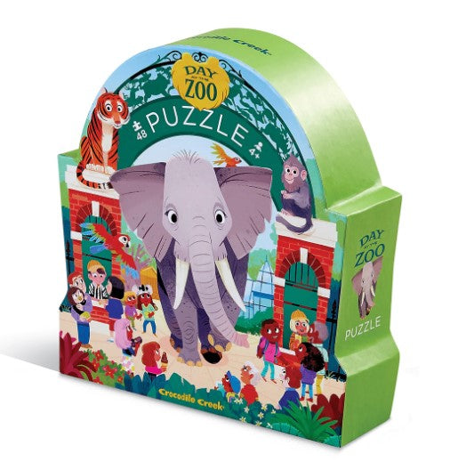 Colorful jigsaw puzzle box titled 'Day at the Zoo' by Crocodile Creek, featuring a cartoon elephant in front of a zoo entrance. The artwork includes various animals and children enjoying their zoo visit.
