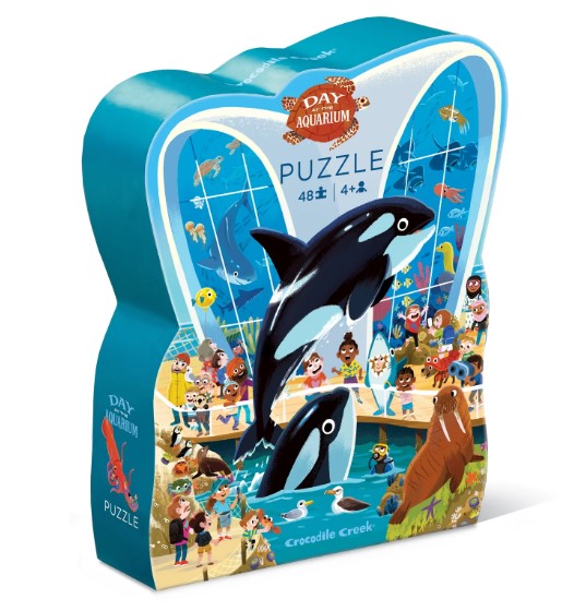 The 'Day at the Aquarium' jigsaw puzzle by Crocodile Creek features a colorful scene depicting various sea animals, including orcas and a walrus, with children and adults enjoying their time at the aquarium. The puzzle comes in a uniquely shaped box, making it an engaging and cute addition for kids aged 4 and up.