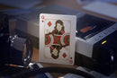 Close-up of a Spider-Man themed playing card featuring a unique design, showcasing a Queen of Diamonds card against a backdrop of vintage photography equipment. The card has intricate graphic details in gold, red, and black, standing out prominently.