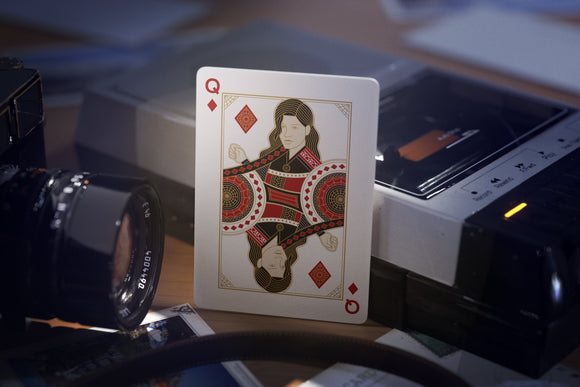 Close-up of a Spider-Man themed playing card featuring a unique design, showcasing a Queen of Diamonds card against a backdrop of vintage photography equipment. The card has intricate graphic details in gold, red, and black, standing out prominently.