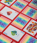 A vibrant display of DKNG Rainbow Wheels Playing Cards laid out on a red background. The deck features colorful designs of bicycles and unique illustrations on the face cards, showcasing a lively and artistic aesthetic ideal for card games.
