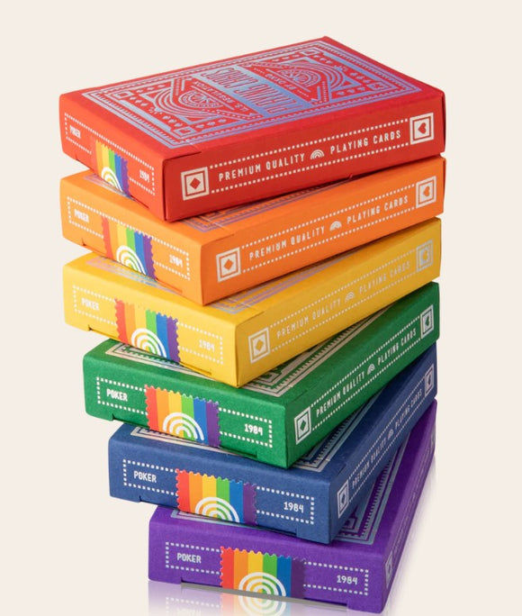 A colorful stack of DKNG Rainbow Wheels Playing Cards by Art of Play. The boxes are displayed in vibrant rainbow colors including red, orange, yellow, green, blue, and purple. Each box is designed with intricate patterns and labeled with 'Premium Quality Playing Cards' and 'Poker' alongside the year '1984.' Perfect for card games and collectors.