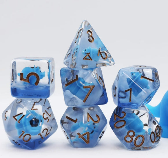 A vibrant Blue Triceratops RPG Dice Set by Foam Brain. The set includes six polyhedral dice featuring a striking blue color with swirled patterns and gold numbering. Each die showcases a small triceratops figure encapsulated within, enhancing their playful and thematic design, perfect for tabletop gaming enthusiasts.