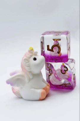 The Mystic Unicorn RPG Dice Set features whimsical designs with a playful unicorn figurine sitting beside sparkly purple dice featuring numbers 3, 4, 5, and 6. The set adds enchantment to any tabletop RPG experience, enhancing gameplay with its unique aesthetics.