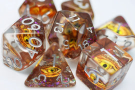 A close-up view of the Golden Dragon Eye RPG Dice Set by Foam Brain. The set features beautifully crafted, translucent dice with intricate golden dragon eye designs and shimmering effects. Various polyhedral shapes, including d20, d12, and d6, display silver numbers for easy reading, perfect for enhancing your tabletop gaming experience.