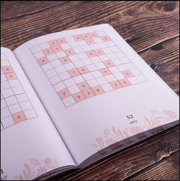 Open book page displaying a Sudoku puzzle. The grid shows several numbers filled in, along with empty boxes outlined in pink. The bottom corner indicates the puzzle is rated as "easy." A floral design is subtly featured along the edges of the page, adding a vintage touch to the overall aesthetic.