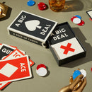 A Big Deal Giant Playing Cards set displayed on a table. The box features a large heart symbol on the front, while the cards inside include various designs like an Ace and a Queen. Colorful poker chips scattered around enhance the gaming atmosphere. The playing cards and packaging are stylishly designed, ideal for fun gatherings or game nights.