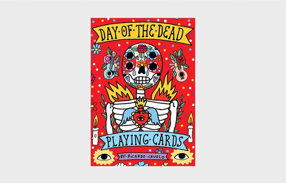 Colorful packaging of the Day of the Dead Playing Cards designed by Ricardo Cavolo. The design features a vibrant skeleton surrounded by flowers, candles, and other festive elements against a bright red background.