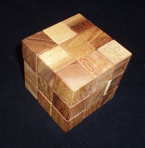 Coffin's Four-Piece Cube by Bill Sheckles, a mechanical puzzle made of various shades of wood, intricately designed with a symmetrical cube shape featuring interlocking pieces that challenge problem-solving skills.