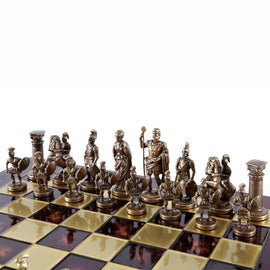 An 11-inch chess set featuring intricately designed brass and gold pieces representing Greek and Roman figures. The chessboard has alternating black and gold squares, with the pieces arranged in two rows. The detailed craftsmanship highlights warriors, emperors, and columns, creating a classic historical theme for gameplay.