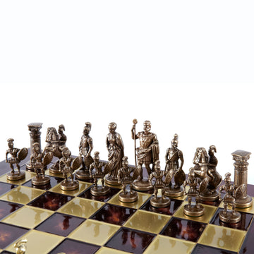 An 11-inch chess set featuring intricately designed brass and gold pieces representing Greek and Roman figures. The chessboard has alternating black and gold squares, with the pieces arranged in two rows. The detailed craftsmanship highlights warriors, emperors, and columns, creating a classic historical theme for gameplay.