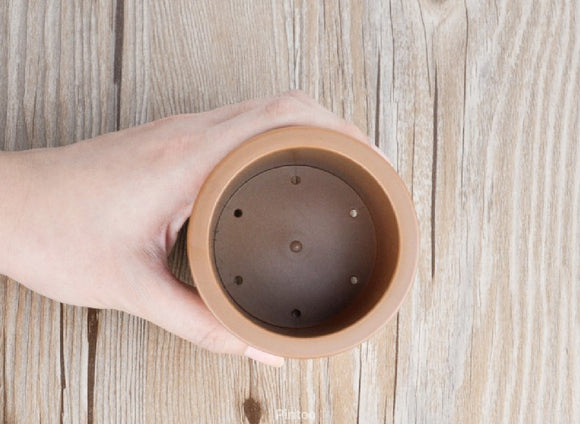 A hand holding the top view of a brown 3D jigsaw puzzle flower pot. The pot has holes in the base and is crafted to resemble a real flower pot. Ideal for puzzle enthusiasts, this unique piece combines creativity and fun.