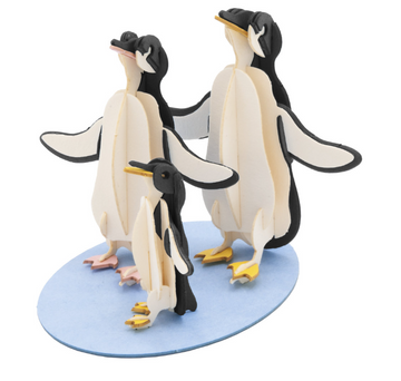 A colorful 3D paper model of a penguin family, including two adult penguins and one chick. The adult penguins have their wings spread out, while the chick stands between them on a light blue base, showcasing intricate design and vibrant colors.