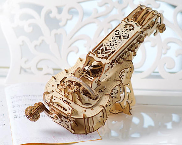 The UGears 3D Hurdy-Gurdy is an intricate wooden DIY kit featuring detailed laser-cut designs. The model showcases elegant woodwork with decorative patterns and mechanics that mimic the traditional musical instrument. The product is placed on a light surface next to sheet music, emphasizing its musical theme and craftsmanship.
