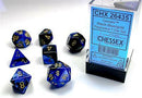 A set of Gemini Black-Blue/Gold Polyhedral RPG dice from Chessex, featuring seven dice in various shapes including a D20 and a D4. The dice have a shiny black and blue finish with gold numerals, displayed in a clear box with a label.