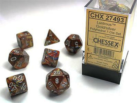 A lustrous gold and silver polyhedral dice set displayed with numbers on each die, featuring a range of shapes including d4, d6, d8, d10, d12, and d20. The set is packaged in a clear box with a yellow label indicating it's from Chessex. The dice have a shimmering, metallic finish that reflects light, making them visually striking and perfect for tabletop gaming.