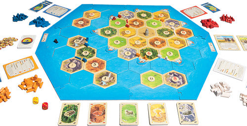 Catan: Seafarers board game featuring a colorful hexagonal game board with various terrains, player pieces in blue, red, yellow, and orange, resource cards, dice, and development cards arranged around the board, all set on a white background.