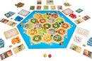 Catan: Traders & Barbarians game by Asmodee, featuring a colorful hexagonal board, player pieces in various colors, resource cards, development cards, and dice, set up for gameplay.
