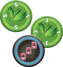 Close-up of game tokens from Jaipur (New Edition) by Space Cowboys, featuring circular tokens with green tea leaves and colorful illustrations of stamps, indicating points in the game. The tokens are designed for a fast-paced two-player card game focused on trade.