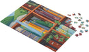 A colorful jigsaw puzzle titled 'Richness' by Asmodee depicting a cozy bookshelf filled with books and surrounded by green plant life. Several puzzle pieces are scattered around the partially completed puzzle.