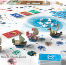 A vibrant tabletop game setup of Namiji by FunForge, featuring intricate game pieces including colorful ships and cards laid out on a stylized board depicting waterways and islands. The scene showcases various mechanics, cards, and tokens, emphasizing the game's strategic and artistic elements. Note: miniatures do not come painted.