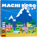 Machi Koro 5th Anniversary Edition game box featuring a colorful and whimsical cityscape with buildings, mountains, and a blue sky. The box design includes a variety of illustrations such as amusement structures and landmarks, representing the vibrant gameplay of city building and strategy.