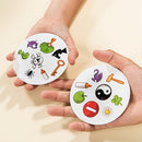 Two hands holding circular cards from the Spot it! game by Zygomatic. Each card features a variety of colorful images including a spider, a key, a green creature, and a yin-yang symbol. The game encourages players to quickly spot matching symbols between cards, promoting fast visual recognition and reaction skills. Perfect for family game nights, parties, or casual fun.
