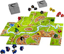 The Carcassonne 20th Anniversary board game by Z-Man showcases beautifully illustrated tiles featuring green hills, rivers, and medieval towns. Various player meeples are displayed in red, yellow, green, and black, while a stack of expansion tiles waits to enhance gameplay. This strategic tile-placement game invites players to build landscapes and compete for points.