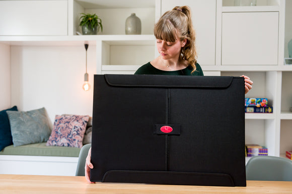 A woman holding the PortaPuzzle Standard, a black jigsaw puzzle storage board designed for 1500 pieces, showcasing its sleek design and functional features in a cozy room setting.