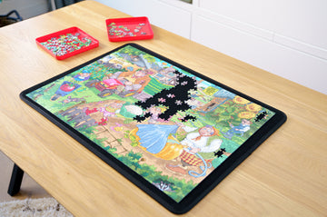 A colorful jigsaw puzzle board set up on a wooden table, featuring an intricate scene with characters and vibrant nature elements. Several puzzle pieces are arranged on the board, with some missing, and trays with additional pieces are placed nearby.