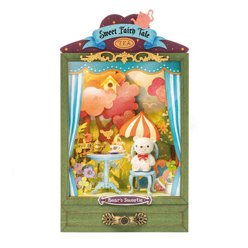 Bear's Sweetie DIY kit by Robotime features a charming scene with a small table set for tea, a cute teddy bear sitting on a blue chair, and colorful, whimsical surroundings including flowers and a bright colored umbrella. The design is framed in a decorative green border with fairy tale motifs.