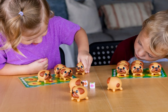Two children playing the game 'Tongues Out!' by Blue Orange U.S.A. They are engaged in stacking and arranging cute dog figurines on a colorful game board. The game includes dice and multiple dog pieces in various positions, showcasing a fun and interactive gameplay experience.
