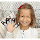 A young girl smiling while holding up her hand, with finger puppets of penguins on each finger. She has a red hair bow and wears a white shirt with colorful buttons. The background features a patterned design.