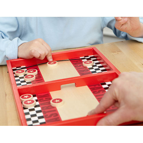 Two players engaged in a fast-paced game of Fastrack by Blue Orange U.S.A. The vibrant red game board features checkerboard patterns and star-marked pucks as they strategically aim to score points by sliding pucks into their opponent's area. A child’s hand is visible, focusing on the gameplay, while an adult hand assists in the game mechanics.