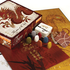 Tsuro board game by Calliope, featuring a beautifully designed box with a red dragon motif. The game includes colorful playing pieces and cards on a decorative game board. The rules are visible on one of the cards, surrounded by intricate designs.