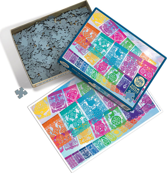 The Cobble Hill Papier Picado jigsaw puzzle box featuring vibrant illustrations. The lid displays intricate designs in various colors, while the base shows numerous jigsaw pieces. A color illustration of the completed puzzle is laid beside the box, showcasing bright artwork inspired by traditional papel picado decorations. Perfect for puzzle enthusiasts and art lovers alike.