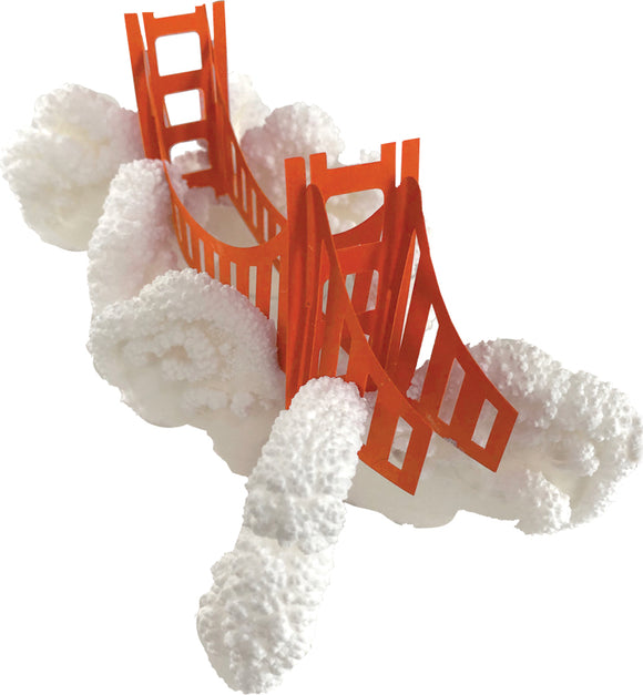 A vibrant Crystal Growing kit featuring a model of the Golden Gate Bridge in bright orange, set on a textured white surface representing clouds. This DIY kit allows kids to create beautiful crystal formations while learning about the science of crystallization.