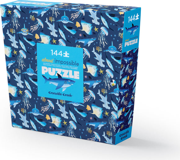 Shark Reef: Almost Impossible Puzzle box featuring vibrant illustrations of various sharks and sea creatures, designed by Crocodile Creek. The package is colorful with blue tones and playful designs, perfect for puzzle enthusiasts.