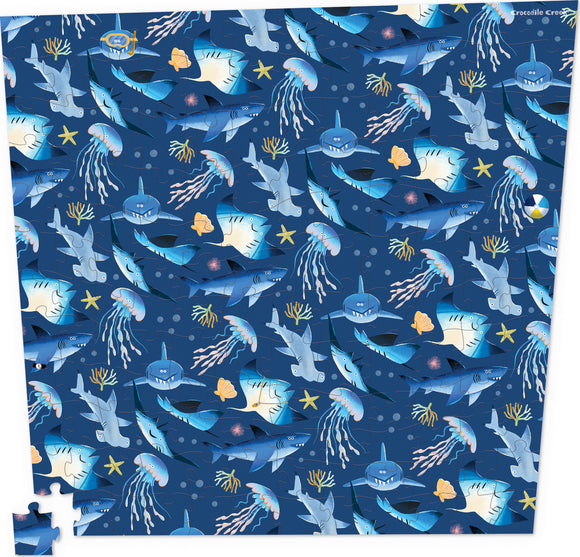 Crocodile Creek's Shark Reef: Almost Impossible Puzzle featuring a vibrant underwater scene filled with various sharks and jellyfish on a deep blue background. The 144-piece jigsaw puzzle showcases colorful marine life including starfish and corals, perfect for puzzle enthusiasts and ocean lovers alike.