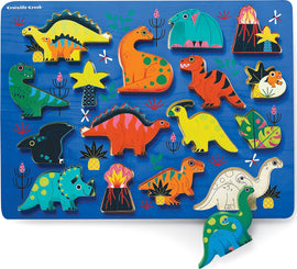 A colorful wooden jigsaw puzzle featuring a variety of dinosaurs and lush plants. The puzzle includes vibrant dinosaur shapes like T-Rex, Triceratops, and more, set against a blue background with artistic details such as flowers and a volcano.